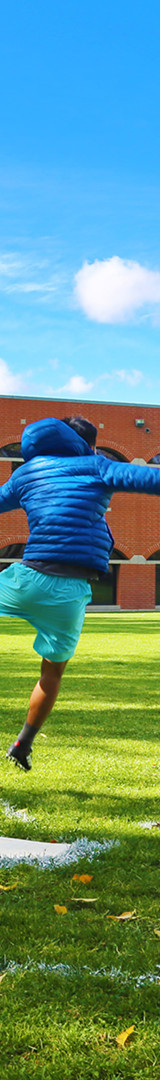 Students playing kickball under a blue sky on campus